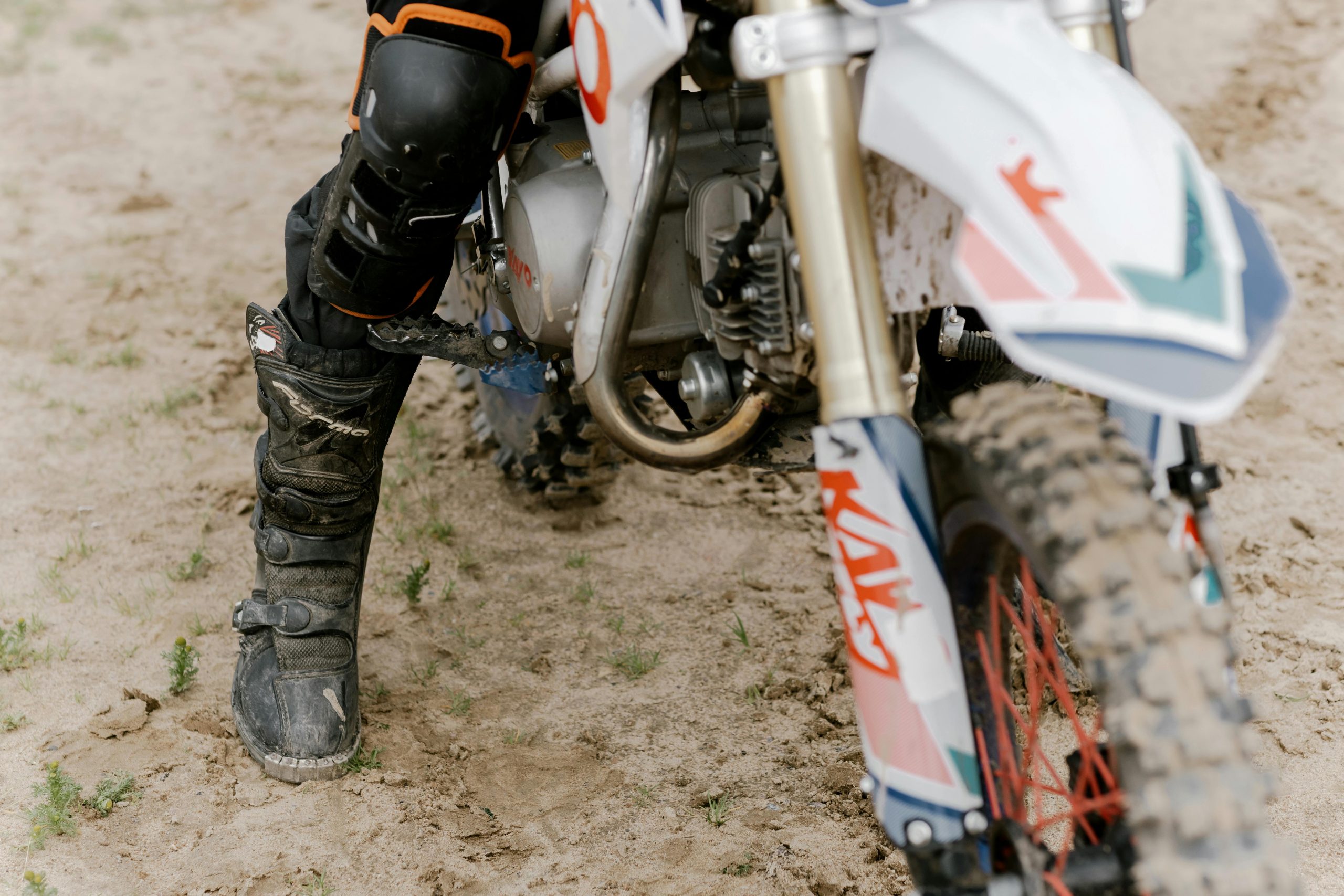 Detailed view of a dirt bike and rider's gear on a sandy trail, showcasing adventure sports.